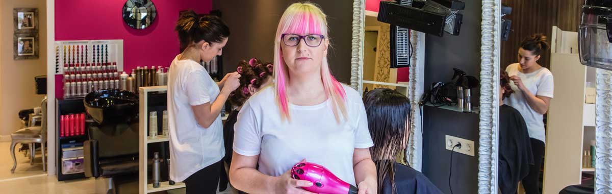 Image of a hairdresser, with pink hair, standing in her salon, illustrating that hairdressers are typical customers of GK Taxation Services